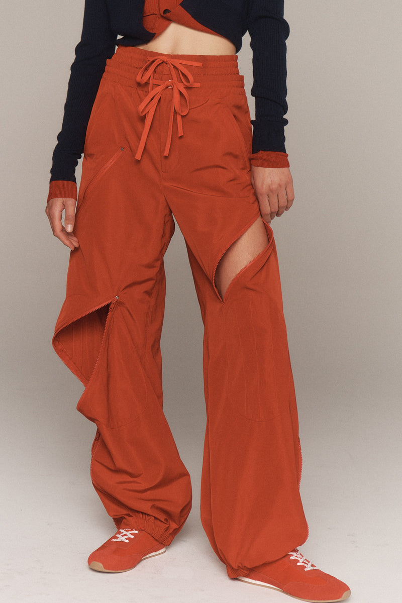MONSE Resort 2026 collection lookbook image of a model wearing rust-colored wide-leg pants with a cutout design on a plain background