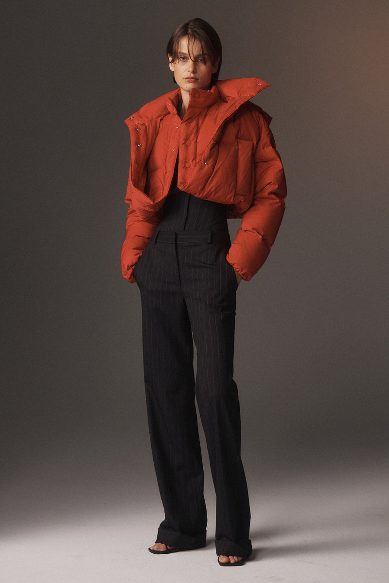 MONSE Resort 2026 collection lookbook image of a model wearing a red puffer jacket and black pants against a gray background