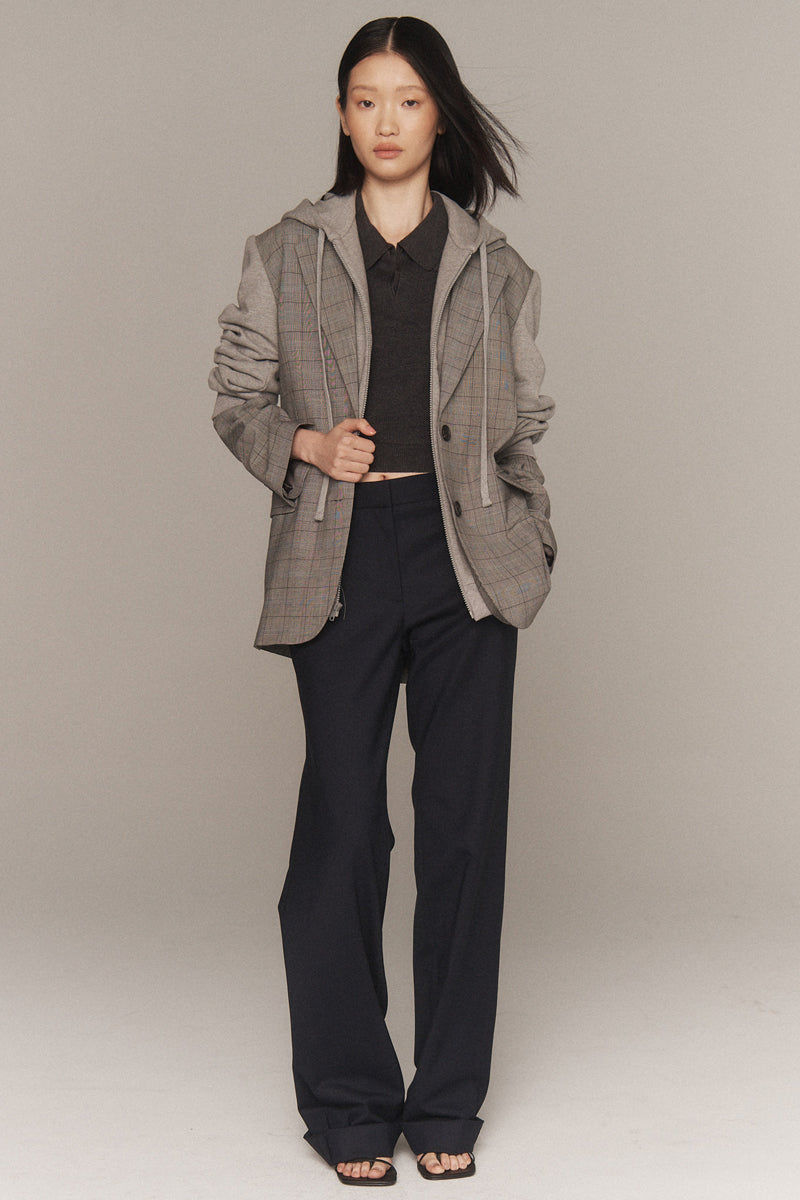 MONSE Resort 2026 collection lookbook image of a model wearing a gray checkered jacket over a black top and pants on a beige background