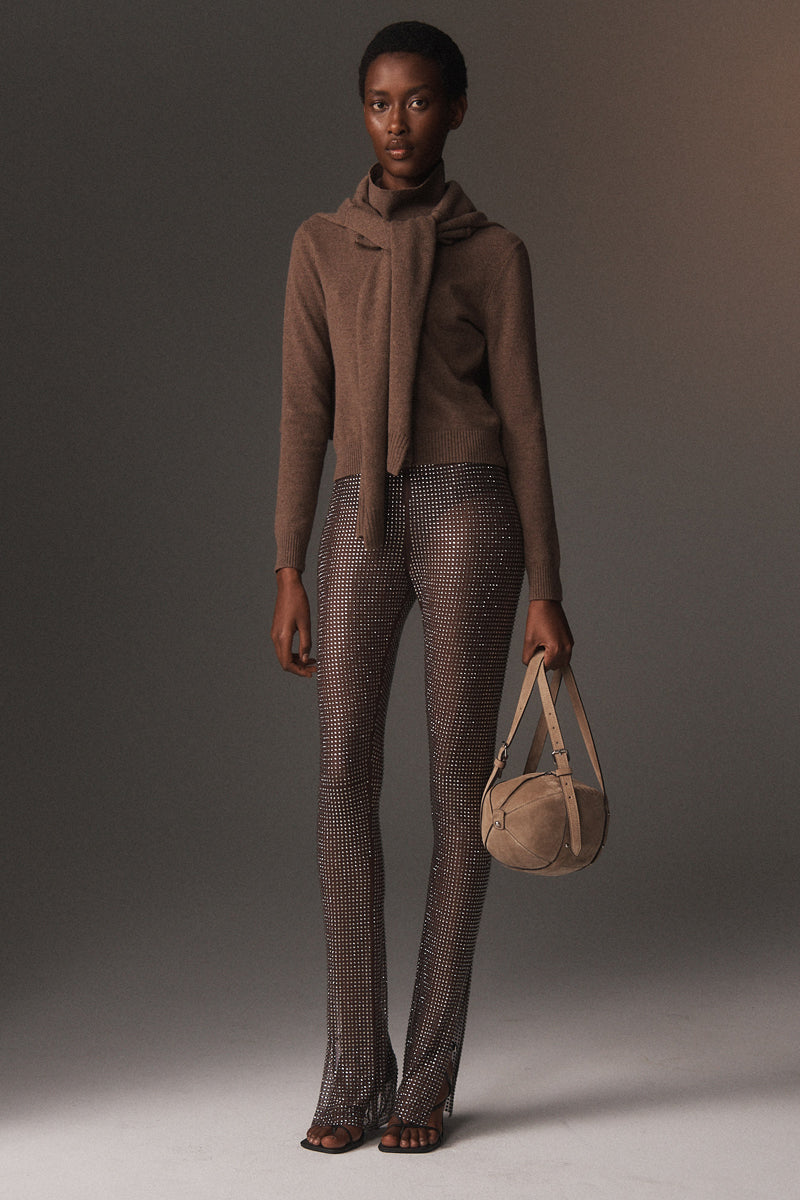 MONSE Resort 2026 collection lookbook image of a model in brown outfit holding a beige handbag against a gray background