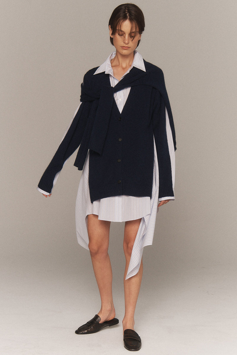 MONSE Resort 2026 collection lookbook image of a model wearing a navy cardigan over a white dress on a plain background