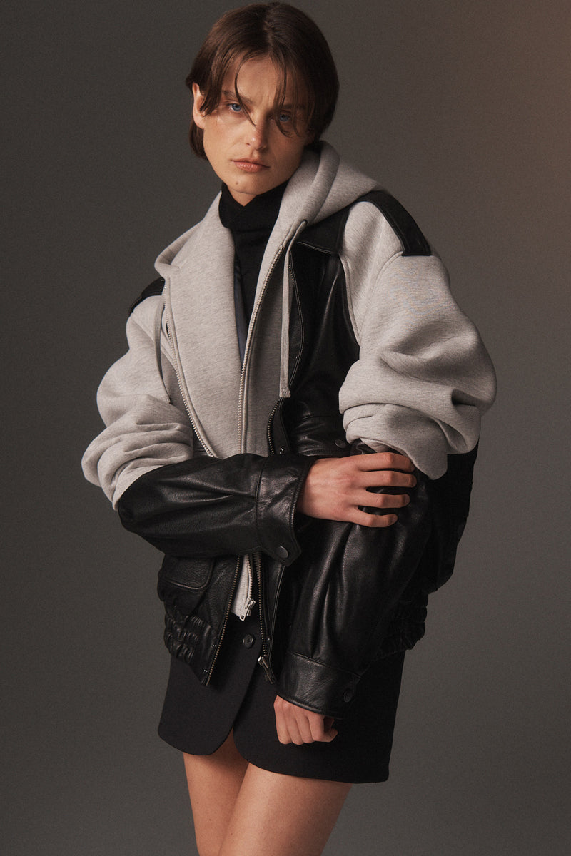 MONSE Resort 2026 collection lookbook image of a model wearing a gray and black outfit with a dark background