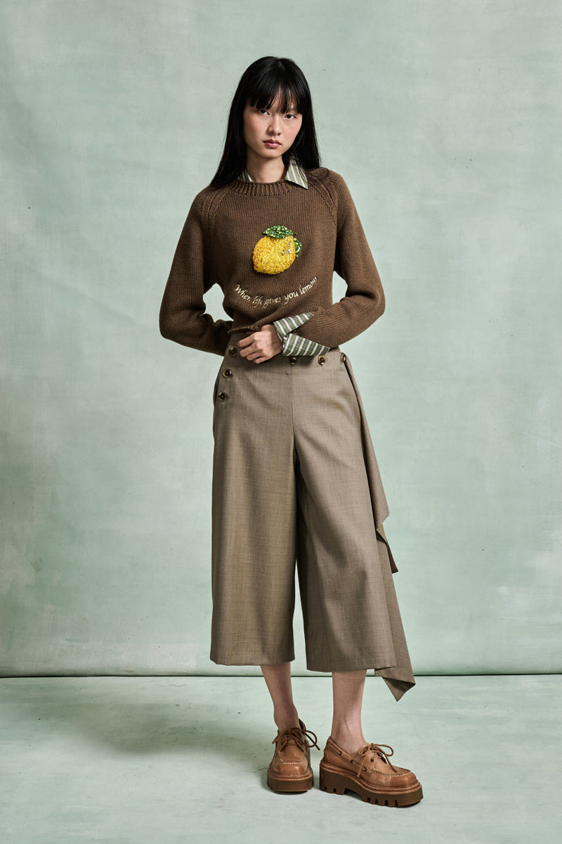 MONSE Spring 2026 Collection look 12 person wearing a brown sweater with a pineapple design and beige pants against a light gray background