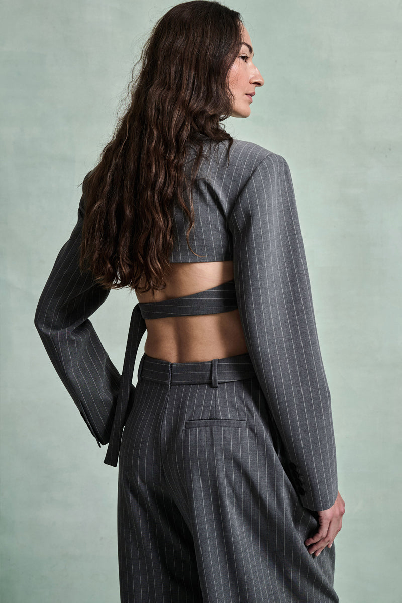 MONSE Spring 2026 Collection look 5 woman wearing a gray pinstripe suit with a cut-out design on a light green background