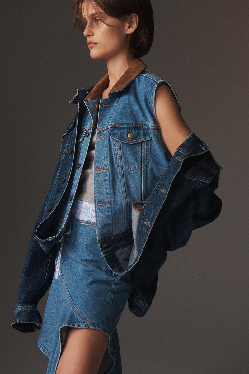 MONSE Resort 2026 collection lookbook image of a model wearing a denim jacket and skirt on a dark background