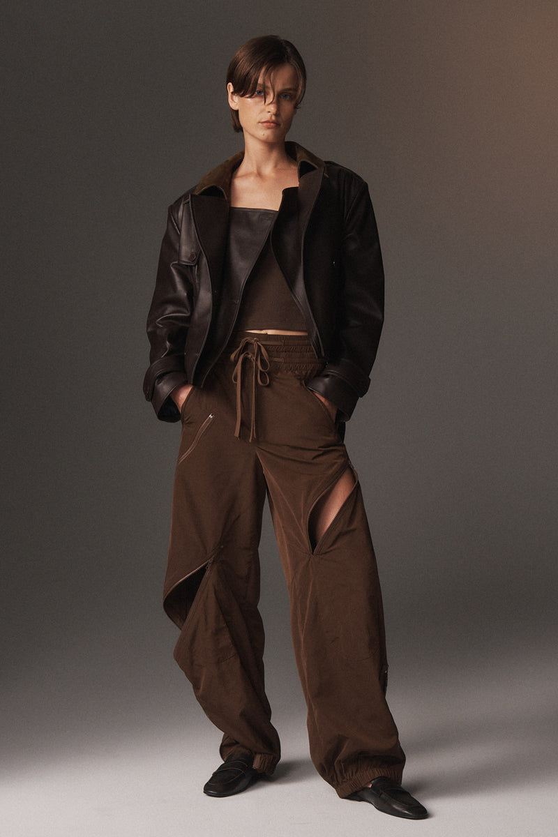 MONSE Resort 2026 collection lookbook image of a model wearing a brown outfit with a jacket and pants on a plain background