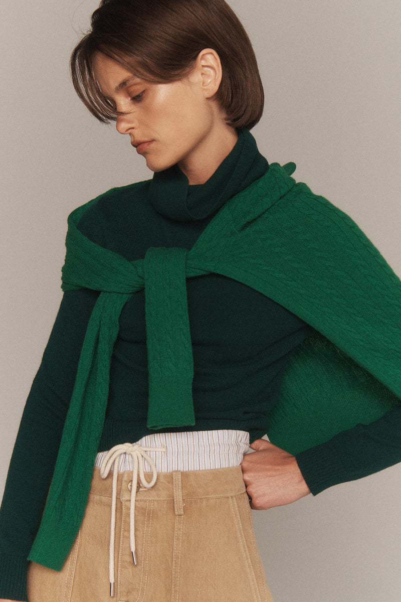 MONSE Resort 2026 collection lookbook image of a model wearing a green scarf and sweater against a plain background