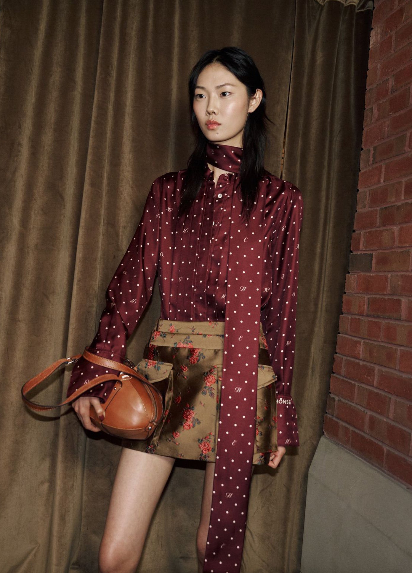 MONSE Tie Neck Cowl Back Blouse in burgundy on model posing in corner
